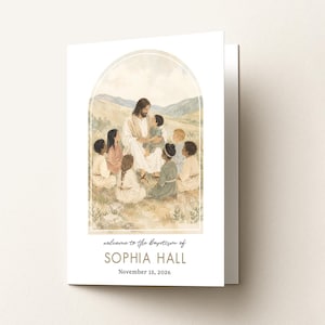 May include: A folded white card featuring a watercolor illustration of a figure in robes surrounded by children in a landscape under an arch. The text reads: welcome to the Baptism of SOPHIA HALL November 15, 2026, in black and tan lettering.