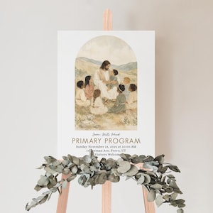 May include: A rectangular sign featuring a watercolor illustration of a figure in robes surrounded by children in a field. Text reads: Seven Hills Ward PRIMARY PROGRAM Sunday November 14, 2026 at 10:00 AM 14 Freeman Ave. Provo, UT Visitors Welcome.
