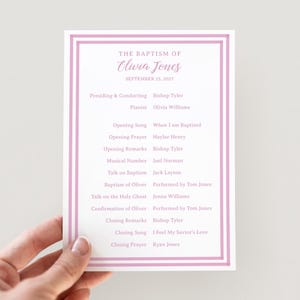 May include: A rectangular baptism program card featuring a light pink double-line border. The text reads: The Baptism of Olivia Jones, September 25, 2027, followed by a list of ceremony participants, musical numbers, and prayers in pink font.