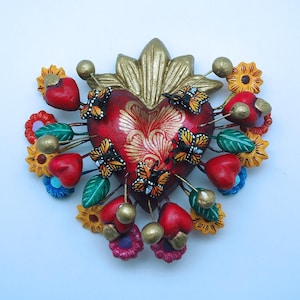 May include: A red heart with gold accents and a floral design, surrounded by small red hearts, butterflies, and flowers. The heart is made of clay and has a rustic, handmade look.