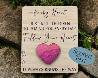 Könnte beinhalten: Ein Holzschild mit dem Text "Lucky Heart" und "Just a little token to remind you every day Follow Your Heart" und einem pinkfarbenen Herz mit Glitzer. Der Text "Scored Text" befindet sich auf einem blauen Oval.