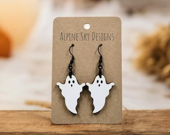 May include: A pair of white ghost-shaped dangle earrings with black hooks. The earrings are on a brown card with the text "Alpine Sky Designs".