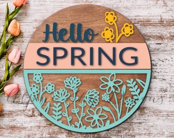 May include: A round wooden sign with the text "Hello Spring" in blue lettering on a pink background. The bottom half of the sign features a teal circle with a floral design.