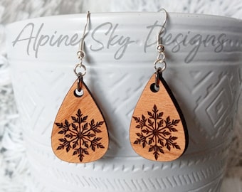 May include: A pair of wooden teardrop-shaped earrings with a laser-cut snowflake design. The earrings are made of light brown wood and have silver hooks.