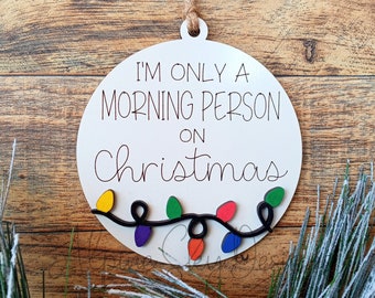 May include: White round Christmas ornament with the text "I'm only a morning person on Christmas" and a string of colorful lights.