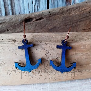 May include: A pair of blue and black anchor earrings with copper hooks. The anchors are made of wood and have a gradient color effect.