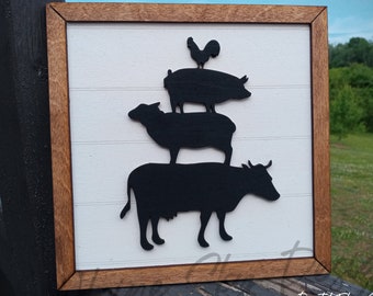 May include: A white wooden sign with a brown frame features a black silhouette of a cow, sheep, pig, and rooster stacked on top of each other. The sign has a farmhouse style.
