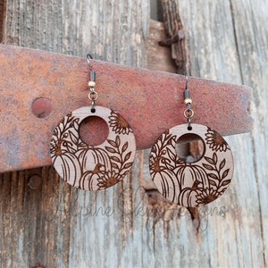 May include: A pair of wooden earrings with a pumpkin and sunflower design. The earrings are round and have a hole in the center. The design is laser-cut into the wood.