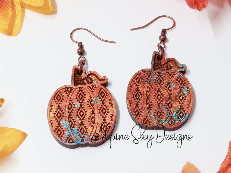 Peut inclure: Une paire de boucles d'oreilles en bois en forme de citrouille avec un crochet en fil de cuivre. Les citrouilles sont peintes avec un motif marbr&eacute; brun, orange et bleu et ont un motif g&eacute;om&eacute;trique grav&eacute; &agrave; la surface. Les boucles d'oreilles sont &eacute;tiquet&eacute;es "Alpine Sky Designs".