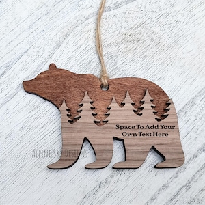Puede incluir: Adorno de madera con forma de oso con un dise&ntilde;o recortado de pinos. El adorno es de dos tonos, con una parte superior marr&oacute;n oscuro y una base marr&oacute;n claro. El texto en el adorno dice "Space To Add Your Own Text Here". Se adjunta una cuerda para colgar.