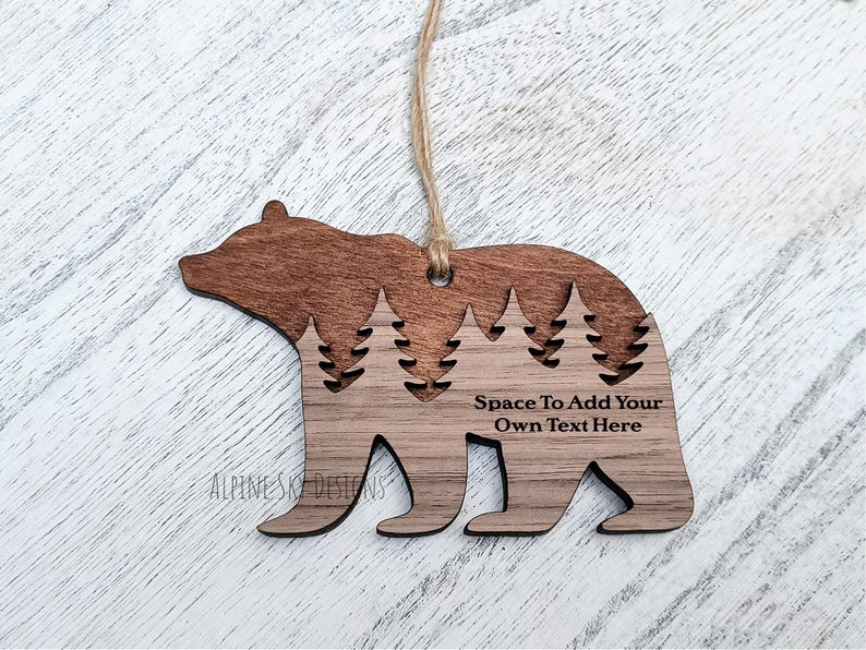 Puede incluir: Adorno de madera con forma de oso con un dise&ntilde;o recortado de pinos. El adorno es de dos tonos, con una parte superior marr&oacute;n oscuro y una base marr&oacute;n claro. El texto en el adorno dice "Space To Add Your Own Text Here". Se adjunta una cuerda para colgar.