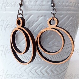 May include: A pair of wooden earrings with a double circle design. The earrings are made of natural wood with a dark brown stain. The earrings are attached to silver hooks.