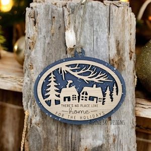 May include: A blue and brown wooden Christmas ornament with a snowy scene and the text "There's no place like home for the holidays - Alpine Sky Designs".