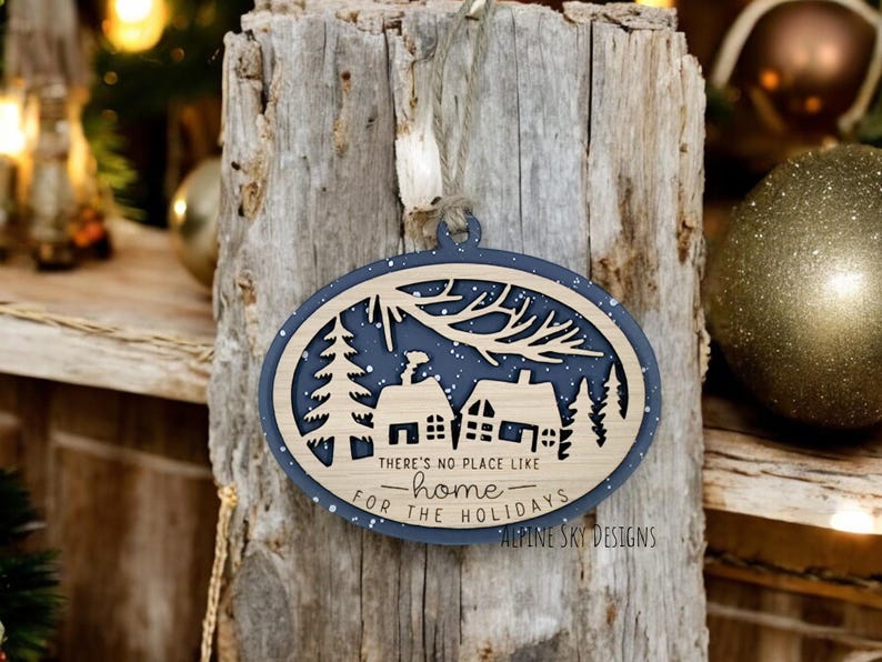 May include: A blue and brown wooden Christmas ornament with a snowy scene and the text "There's no place like home for the holidays - Alpine Sky Designs".