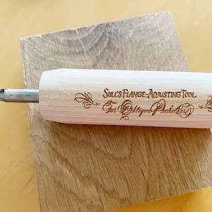 May include: A wooden tool with a metal blade, engraved with the text "Sull's Flange Adjusting Tool for Oblique Plumbing".