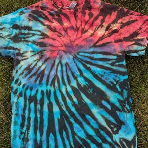 Könnte beinhalten: Ein Batik-T-Shirt mit einem Spiralmuster in Blautönen, Schwarz und Rot.