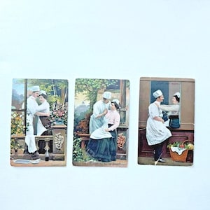 Könnte beinhalten: Drei Vintage-Postkarten mit Paaren in Kochuniformen. Die Karten zeigen romantische Szenen in Außen- und Innenräumen. Die Farbpalette umfasst Weiß-, Blau-, Grün- und Brauntöne mit floralen und architektonischen Details.