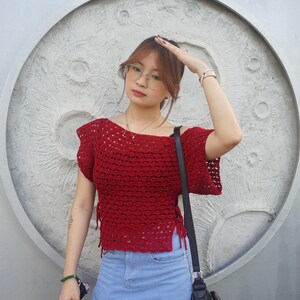 May include: A red crochet top with short sleeves and side ties, paired with a light blue denim skirt. A black shoulder bag is visible. The background features a textured, circular design.