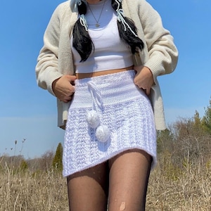 May include: White crochet skirt with a white pom-pom detail. The skirt is mini length and has a high waist.