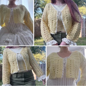 May include: A light yellow crochet cardigan with long sleeves and a tie closure. The cardigan has white lace trim on the cuffs and edges. The open weave design is visible.
