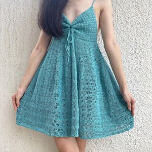Puede incluir: Un vestido de crochet azul claro con cuello en V y tirantes finos. El vestido tiene un corte holgado y una falda fluida.