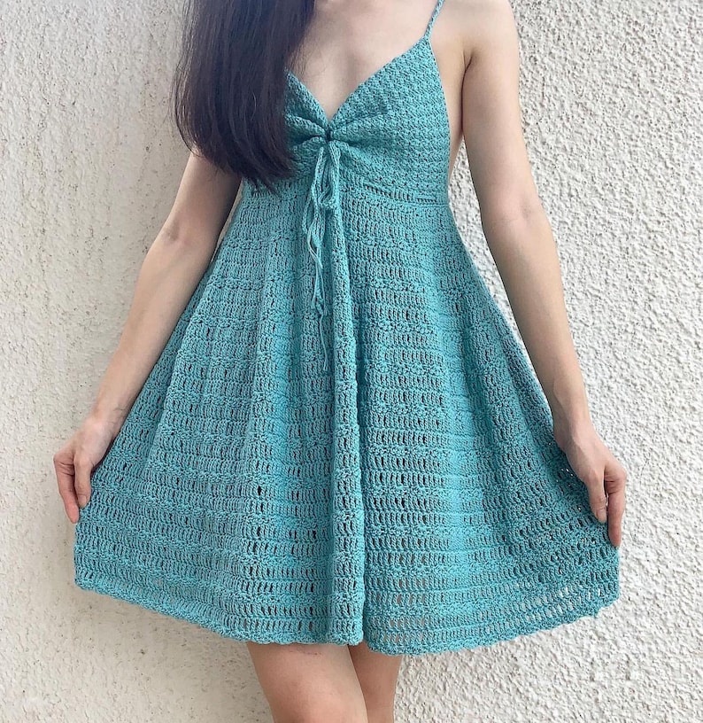 Puede incluir: Un vestido de crochet azul claro con cuello en V y tirantes finos. El vestido tiene un corte holgado y una falda fluida.