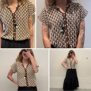 May include: A short-sleeved, button-down crochet top in brown and cream. The top features a V-neck and a repeating pattern. The buttons and trim are brown. The top is paired with a black skirt. The style is vintage.