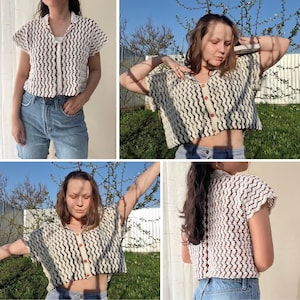 May include: A white crochet top with a brown and black wavy pattern. The top has short sleeves and a button closure. The model is wearing the top with blue jeans.