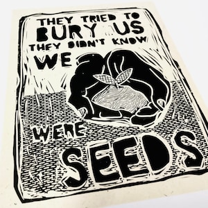 以下が含まれることがあります： 「They tried to bury us they didn't know we were seeds」というテキストが書かれた白黒のプリント。プリントには、小さな植物を持った手が描かれている。