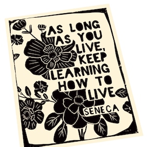 May include: Black and white print with a floral design and the quote "As long as you live, keep learning how to live" by Seneca.