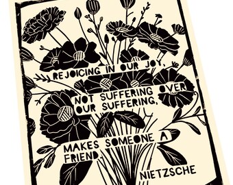 May include: Black and cream-colored art print featuring a floral bouquet and the quote "Rejoicing in our joy, not suffering over our suffering, makes someone a friend" by Nietzsche. The print has a black border.