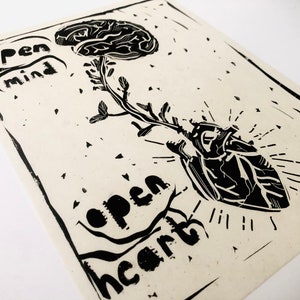 May include: Black and white linocut print with a stylized image of a brain growing from a heart. The text "open mind" is above the brain and "open heart" is below the heart.