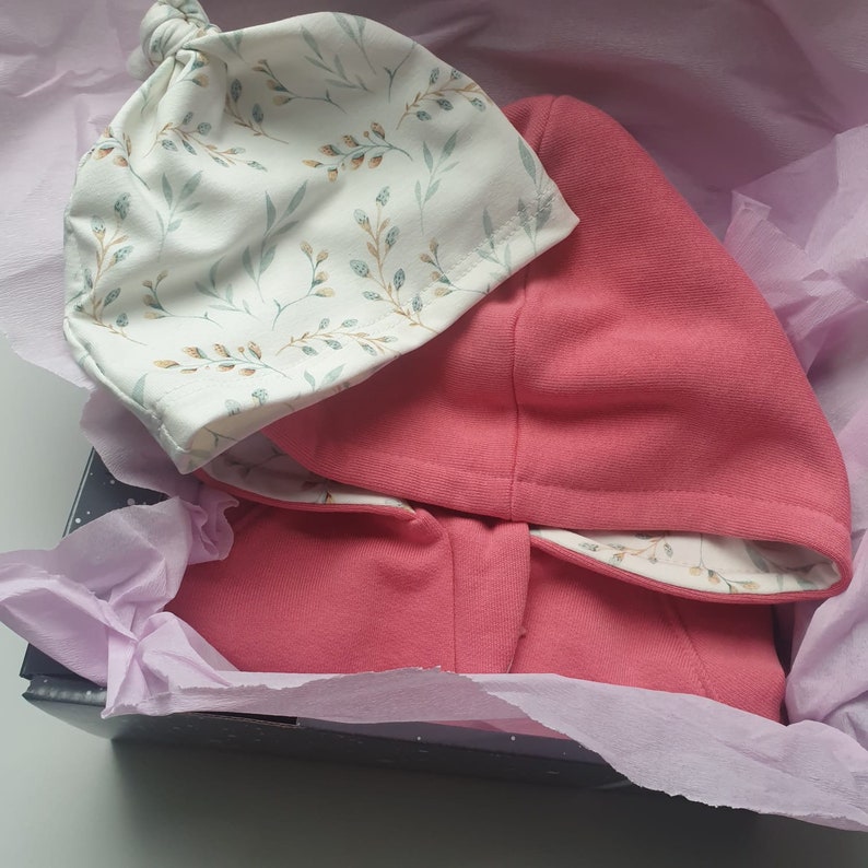 Peut inclure: Un sweat &agrave; capuche rose avec un bonnet blanc &agrave; imprim&eacute; floral. Le sweat et le bonnet sont dans une bo&icirc;te cadeau avec du papier de soie violet.