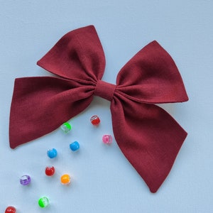 Peut inclure: Un grand nœud en tissu bordeaux avec un nœud central. Le nœud est entouré de perles en plastique colorées.