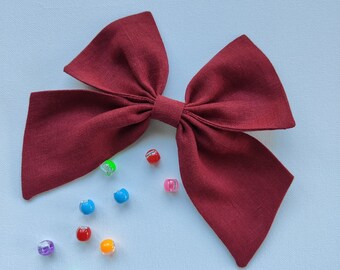 May include: A large burgundy fabric bow with a centre knot. The bow is surrounded by colourful plastic beads.