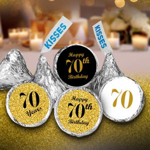 May include: Gold and black round stickers with the text "Happy 70th Birthday" and "70 Years" on a gold glitter background. The stickers are placed on silver foil-wrapped chocolate kisses.