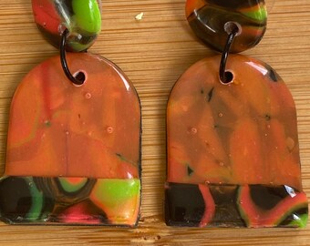 May include: A pair of dangle earrings featuring a circular stud top and a larger arch-shaped drop piece. The earrings are crafted with a marbled pattern in vibrant shades of orange, lime green, black, and red, finished with a glossy, smooth surface.