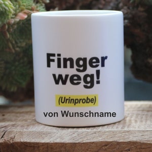 Könnte beinhalten: Weiße Keramiktasse mit schwarzem Text, der "Finger weg! (Urintprobe) von Wunschname" lautet.