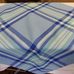 May include: A light blue and white plaid tablecloth with a diagonal pattern. The plaid design incorporates shades of blue and green. The fabric appears to be cotton or a similar material, suitable for casual dining or kitchen use.
