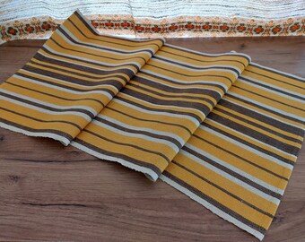 May include: A striped table runner in shades of brown, beige, and yellow. The runner is made of a woven fabric and has a slightly textured surface.