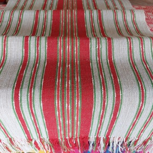 May include: A white table runner with red and green stripes. The runner has a fringe on the ends.