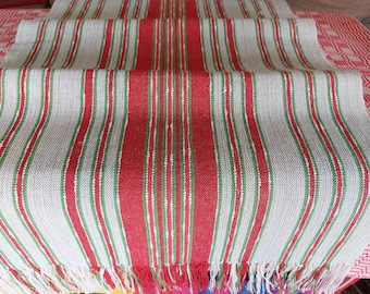 May include: A white table runner with red and green stripes. The runner has a fringe on the ends.