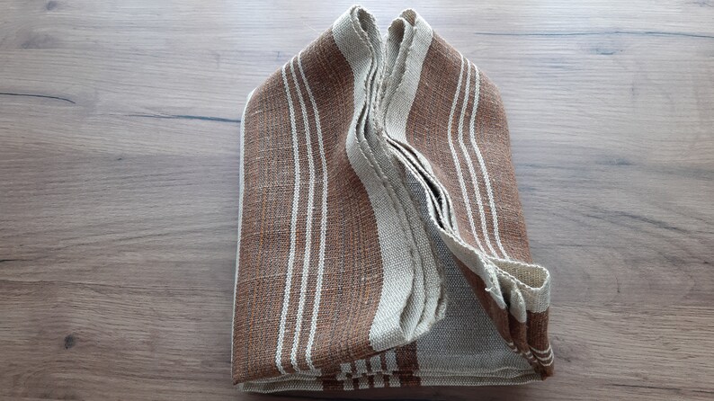 May include: A folded brown and white striped fabric towel. The towel is folded in half and then folded again, creating a rectangular shape.