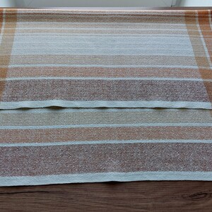 May include: Two rectangular, woven placemats with a plaid pattern. The color scheme includes shades of brown, orange, and cream. The placemats are made of a textured fabric and are suitable for dining or kitchen decor.