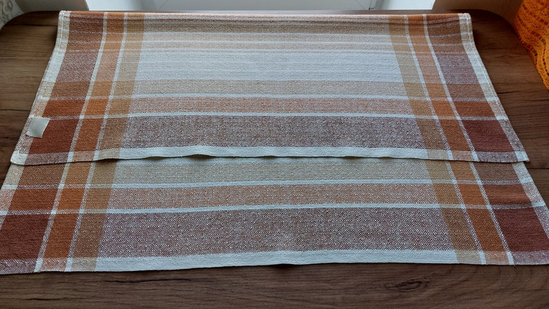May include: Two rectangular, woven placemats with a plaid pattern. The color scheme includes shades of brown, orange, and cream. The placemats are made of a textured fabric and are suitable for dining or kitchen decor.