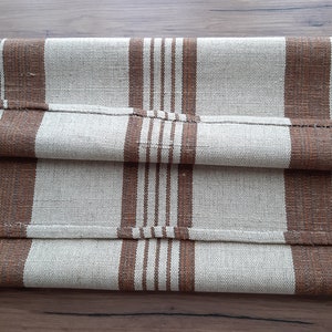 May include: A folded brown and beige striped fabric runner. The runner is made of a woven material and has a subtle texture.