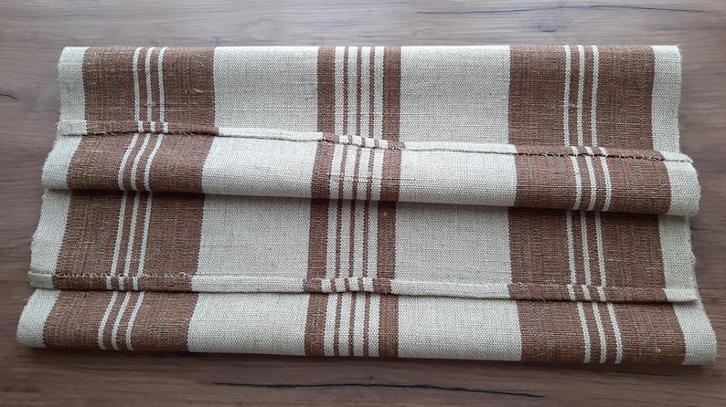 May include: A folded brown and beige striped fabric runner. The runner is made of a woven material and has a subtle texture.