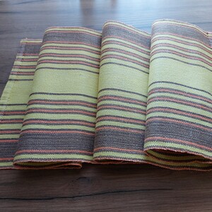 May include: A folded table runner with a striped pattern in shades of green, brown, and orange.