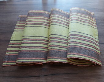 May include: A folded table runner with a striped pattern in shades of green, brown, and orange.