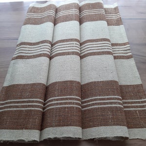 May include: Four brown and white striped linen tea towels. The towels are folded and laid out on a wooden surface.